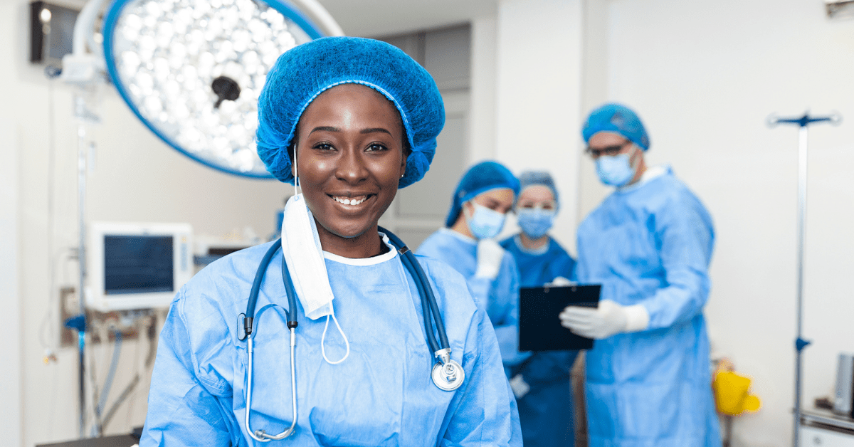 Close-up of a African American surgeon woman looking at camera with colleagues performing in background in operation room. The concept of medicine - stock photo