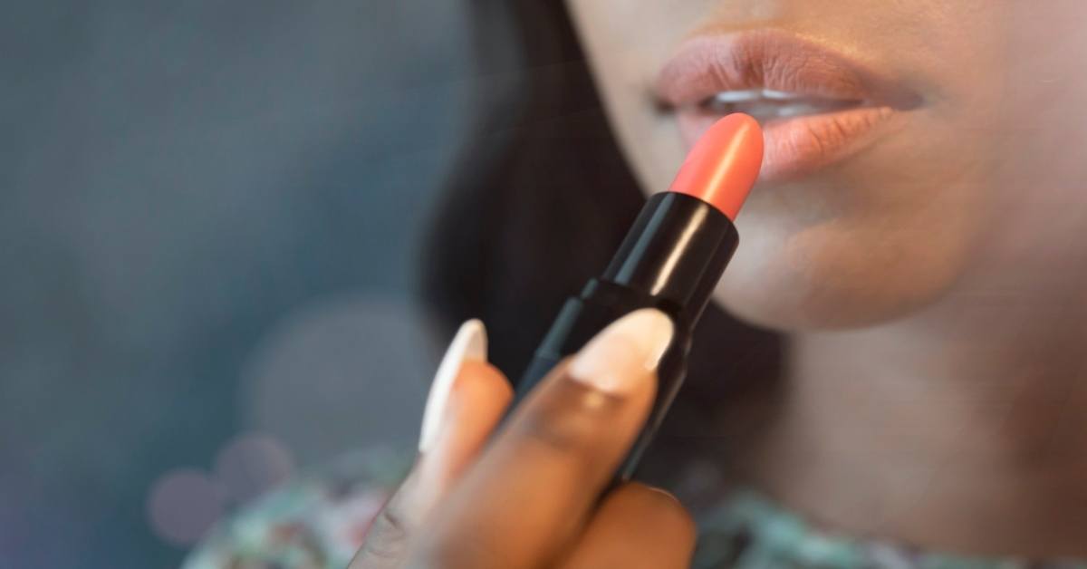 woman putting on coral lipstick/canva