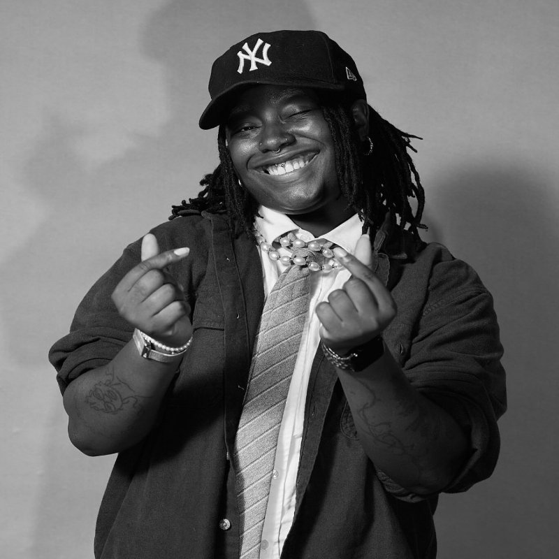 Black lesbian in new York city fitted cap, pearls and button down with tie snapping fingers. 