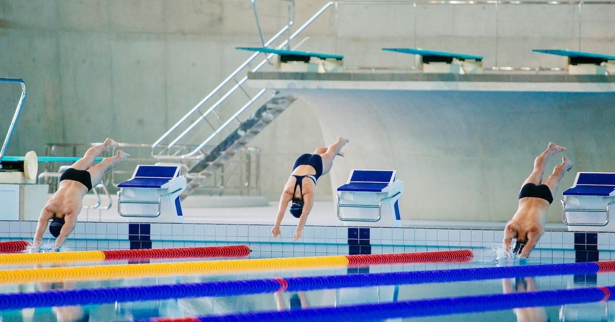 Three people diving into a swimming pool.