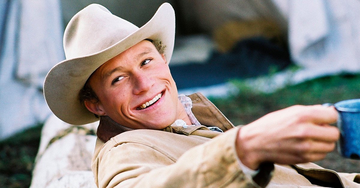 Heath Ledger as Ennis Del Mar looks back smiling holding a mub