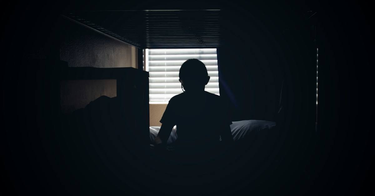 An individual sitting in a bed in a dark room