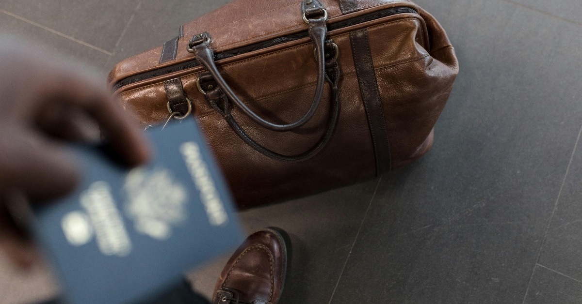 An individual holding a passport with a duffle bag placed on the floor