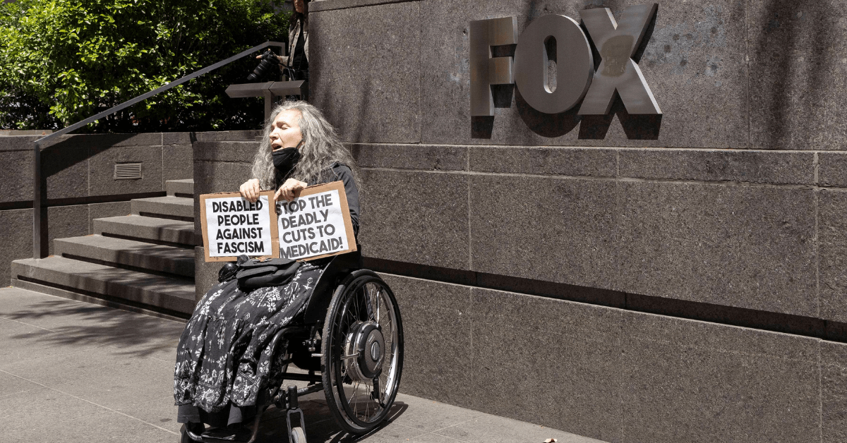 a demonstrator who uses a wheelchair holds signs that read 'STOP DEADLY CUTS TO MEDICAID!' 'DISABLED PEOPLE AGAINST FASCISM'