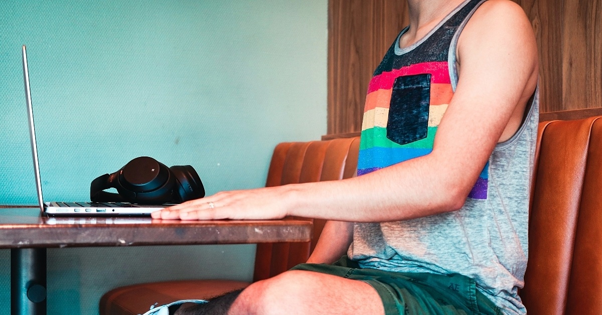 Man wearing pride tank top using laptop