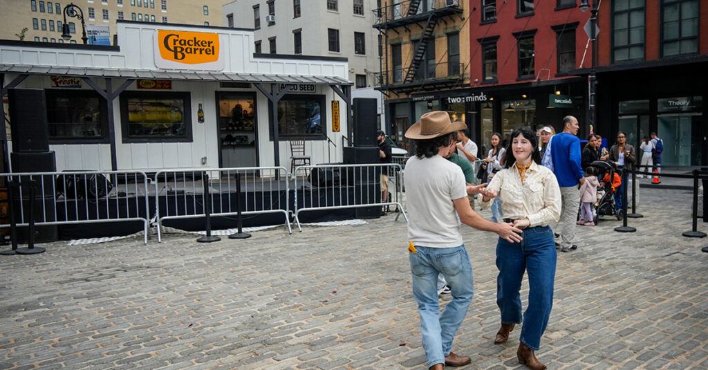 Couple dancing in front of a Cracker Barrel location featuring the new logo, customers lined up for the store