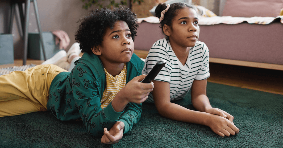 Two African-American children lying on the floor watching TV together