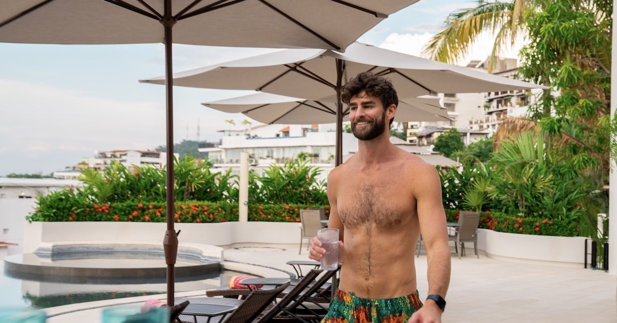A person standing by the pool with a drink.