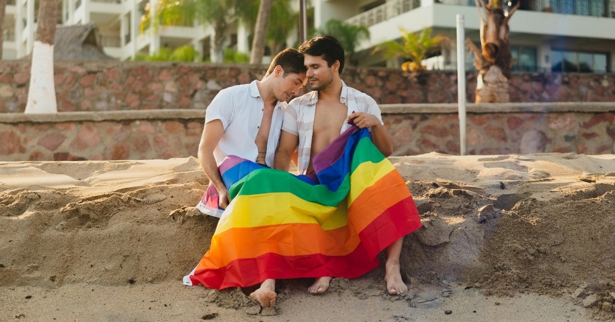A Couple Using a Rainbow Blanket Sitting on Beach Sand
